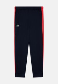 Pantalons de jogging navy avec des rayures latérales rouges. Présente un logo vert sur la jambe gauche. Fabriqués dans un tissu lisse et léger avec un élastique à la taille.