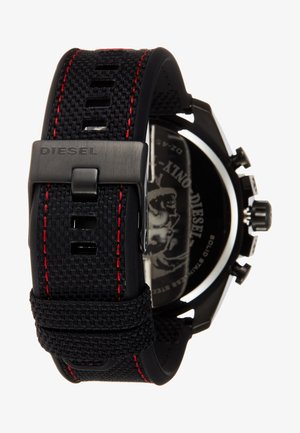Svart vevd stoffklokkerem med røde sømmer, svart metallspenne med innfrest "DIESEL" og en delvis synlig svart klokkehus.