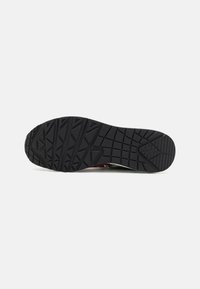 Black rubber outsole with a textured tread pattern, featuring angular shapes and grooves for traction. Designed for durability and grip.