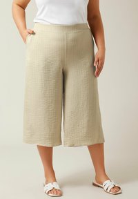 Beige, getextureerde wijde culottes met zijzakken, met een subtiele geruite print en een hoge taille. Gepaard met witte slide sandalen.