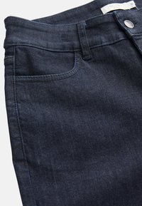 Mörkblå denimjeans i närbild som visar framfickan, bältesöglan, metallknappen och etiketten med texten "CELLBES OF SWEDEN 38."