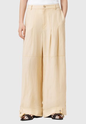 Leveälahkeiset housut pehmeästä beigestä kankaasta, joissa on etutaitokset, korkea vyötärö ja työvaatteista inspiraationsa saanut napit lahkeensuissa.