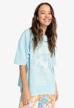 Lysblå oversized T-shirt i blødt bomuld med hvid grafisk tekst og billeder. Parret med blomster-mønstrede, multikolorede bukser.