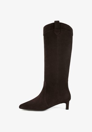 Stivale in suede marrone scuro, alto fino al ginocchio, con punta affusolata, tacco basso a kitten e un pratico linguetta nella parte superiore per facilitarne l'indossamento.