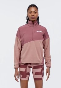 Pitkähihaisessa, vetoketjullisessa pinkki-beige värilohkoista pulloverissa on pehmeä rakenne ja "Terrex"-logo. Yhdistetty saman sävyisiin kuviollisiin shortseihin.