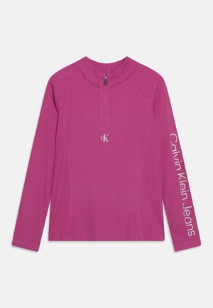 Langärmliges, magentafarbenes, geripptes Oberteil mit Viertelreißverschluss, kleinem "cK"-Logo in der Mitte der Brust und dem Schriftzug "Calvin Klein Jeans" auf dem linken Ärmel.