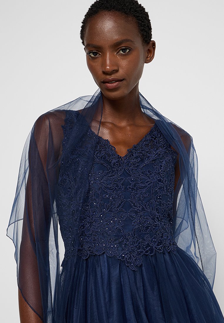 Granatowa suknia z koronkowym górnym zdobieniem w kwiaty i koralikami, z przewiewnym, przezroczystym materiałem nachodzącym na ramiona.