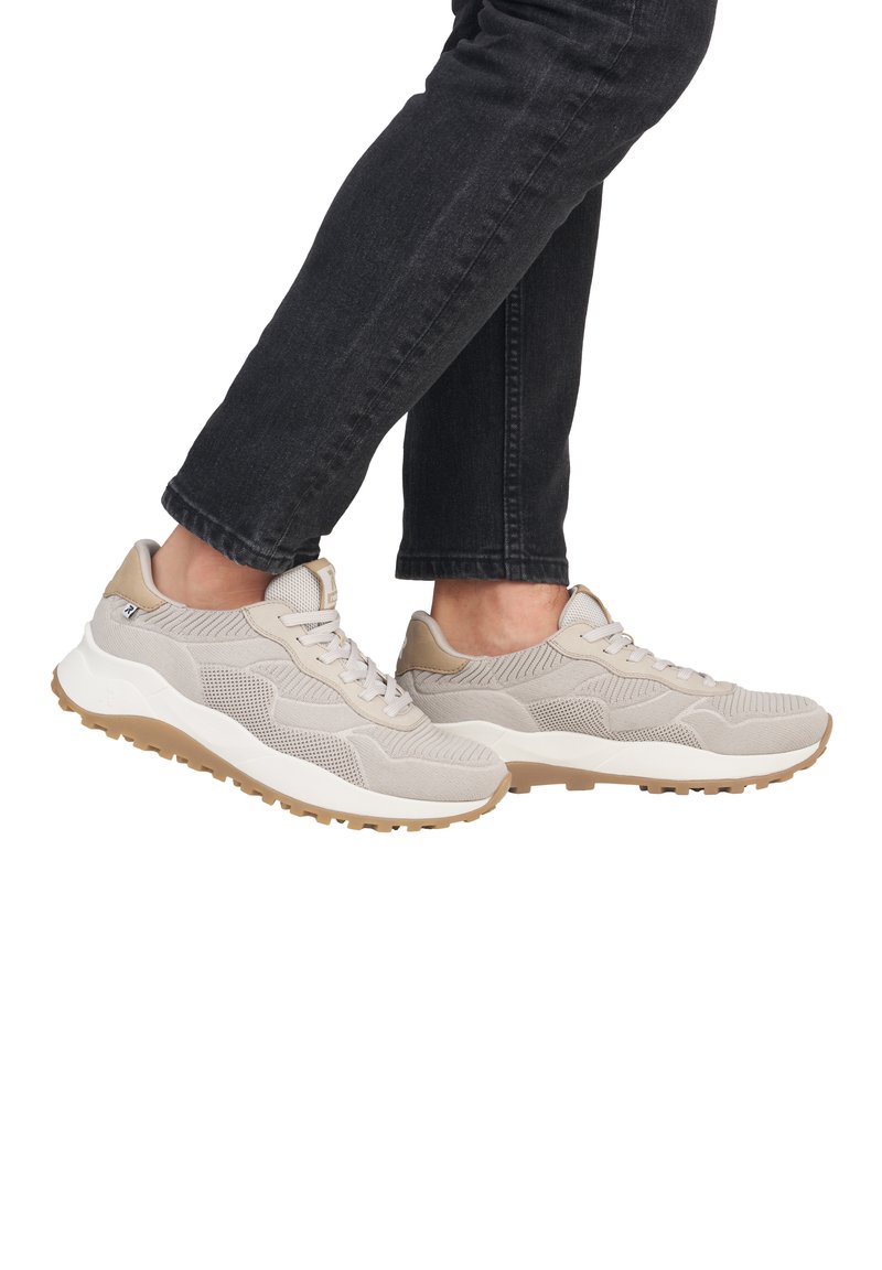 Baskets de sport beiges avec tige en maille texturée, accents en suède et semelle de confort blanche. Stylisées avec un jean sombre, mettant en valeur les chaussures en action.