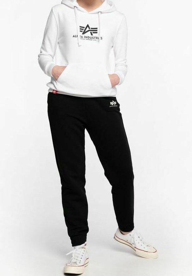 Vit hoodie med en svart logotyp, matchad med svarta sweatpants som har små logotyper. Kläderna är avslappnade och tillverkade av mjukt material.