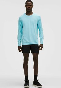 Vaaleansininen pitkähihainen urheilupaita, jossa on teksturoitu kuvio, yhdistetty mustiin shortseihin, mustien sukkien ja lenkkareiden kanssa.