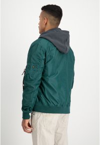 Groene nylon bomberjack met een grijze capuchon, ribbelmanchetten en een ritssluiting pocketdetail op de mouw. Gladde textuur met een aansluitende silhouet.