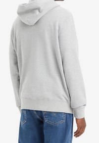 Sudadera de algodón gris con un corte relajado, que presenta una capucha y puños de canalé, combinada con jeans de mezclilla azul. La vista trasera enfatiza la simplicidad y la comodidad.
