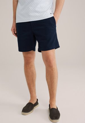 Dunkelblaue Baumwollshorts, normale Passform, seitliche Taschen, umgeschlagene Säume. Getragen mit dunklen Espadrilles, die ein flaches Canvas-Design aufweisen.