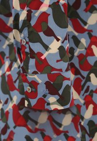 Shirt sleeve with buttoned cuff, covered in a multicolored bird pattern in red, green, cream, and blue tones.