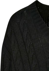 Svart kabelstrikket genser med V-halsdesign, med teksturerte mønstre og ribbestrikkedetaljer ved halsen og ermene.