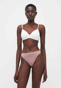 Balta mīksta krūštura ar V formas dizainu un plānām siksnām, apvienots ar gaiši rozā augsto vidukļa bikini apakšdaļu ar gludu tekstūru.