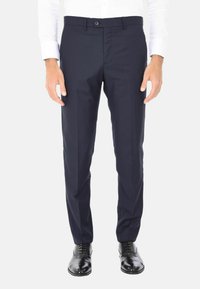 Pantaloni da abito blu navy realizzati in tessuto liscio, con vestibilità sartoriale, chiusura con un bottone e piega frontale. Indossati con scarpe nere.