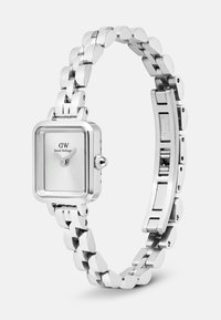 Montre-bracelet carrée en argent de Daniel Wellington avec un cadran minimaliste et un bracelet en acier inoxydable à maillons, montrée partiellement ouverte.