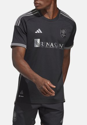 Mand iført sort Nashville SC fodboldtrøje med sponsorlogo og matchende shorts, stående med armen strakt fremad.