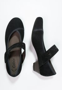 Chaussures en suède noir avec un bout arrondi, un petit talon carré et une sangle ajustable avec des accents brillants. Intérieur doux pour un confort optimal.