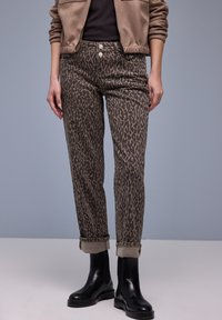 Leopardikuosilliset housut ruskeassa värimaailmassa, pehmeästä kankaasta valmistetut. Istuvuudeltaan kapeat mallit, joissa käännetyt lahkeensuut, yhdistetty mustiin nilkkureihin.