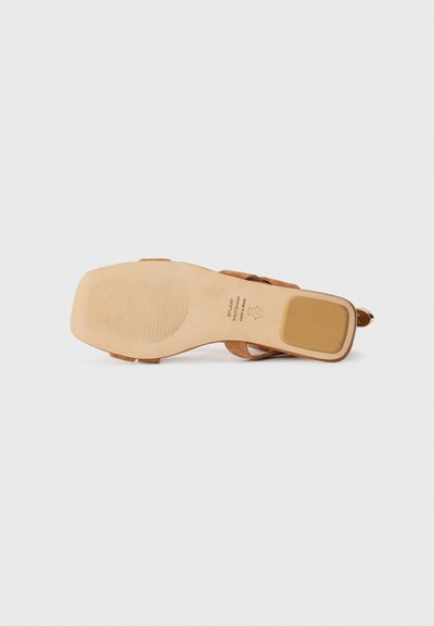 Brun mockasinsandal sula med en slät, beige gummiyttersula. Har ett präglat logotyp och ett texturerat greppmönster för bättre fäste.