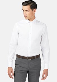 Vit långärmad skjorta med klassisk krage, knappstängning fram och manschetter, ihop med grå byxor och ett brunt läderbälte.