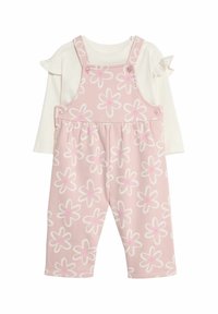Rosa Blumendruck-Latzhose mit Trägern und Knöpfen, kombiniert mit einem weißen Langarmshirt mit Rüschensleeves.
