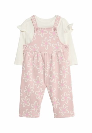 Pantalones de mezclilla rosa con un patrón floral, con tirantes y botones, combinados con una blusa blanca de manga larga con mangas acampanadas.