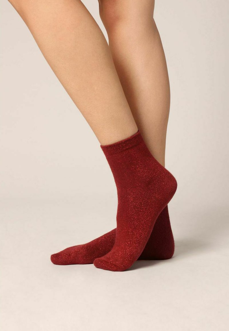 Chaussettes rouges jusqu'à la cheville avec une texture pailletée. Elles sont dotées d'un bord côtelé et d'une section de pied lisse, offrant un ajustement confortable.