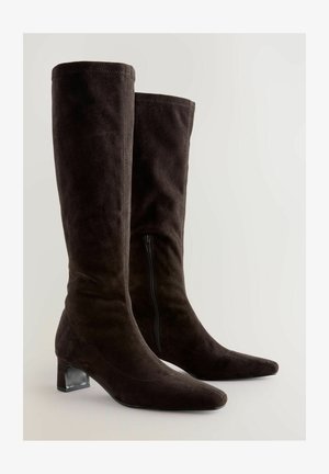Knähöga bruna mockastövlar med spetsig tå, klack med blockform och sidodragkedja. Slät textur med strukturerad design.