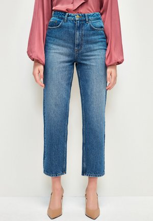 Jeans de denim azul de cintura alta y pierna recta con un acabado desvanecido y dobladillo sin deshilachar. Combinados con una blusa de satén color rosa y tacones beige.