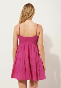 Vestido sin mangas en fucsia con un cuerpo fruncido, volantes en capas y tirantes ajustables, hecho de un tejido ligero con textura suave.