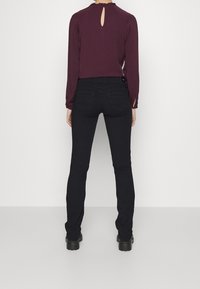 Bordeauxblus med ett nyckelhålssnitt i ryggen, matchad med figurnära svarta jeans och kraftiga svarta stövlar, med en slät yta.