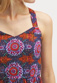 Robe multicolore en tissu bleu foncé avec des motifs floraux et géométriques vibrants, bretelles réglables et corsage ajusté.