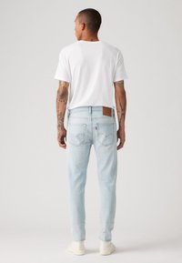 Lys blå denim jeans med rett passform, baklommer og en brun lær lapp. Kombinert med en hvit t-skjorte med korte ermer.