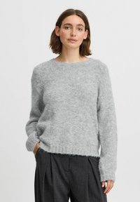 Pull en maille gris clair avec une texture douce, col rond et manches longues. L'ourlet est légèrement plus long à l'arrière.