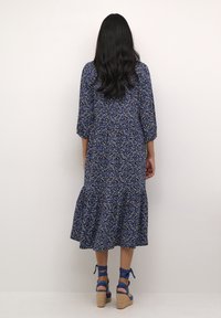 Modré květinové midi šaty s třičtvrtinovými rukávy, volánkovým lemem a strukturovanou tkaninou. V kombinaci s modrými sandály na klínku s kotníkovým řemínkem.