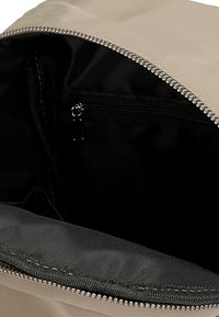 Beżowe wnętrze plecaka z czarną podszewką; zawiera kieszeń na zamek błyskawiczny oraz gładką teksturę materiału. Widoczne detale metalowego zamka.