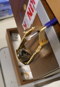 Goldfarbener Edelstahluhren mit einem gemusterten Armband, das ein schwarzes Zifferblatt und gravierte Details auf der Gehäuserückseite zeigt, liegt auf einer hölzernen Oberfläche.