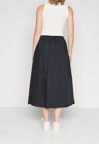 Falda negra hasta los tobillos con cintura elástica, combinada con una camiseta sin mangas blanca y zapatillas blancas. Diseño simple, textura suave.