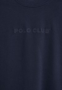 Tissu bleu marine avec col côtelé, arborant l'inscription « POLO CLUB » brodée en fil bleu marine assorti sur la poitrine.
