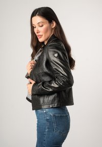 Zwarte leren jas met een fitted ontwerp, drukknopen en een zachte grijze voering. Geaccentueerd met een schildlogo op de linker schouder.