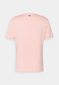 Camiseta de algodón rosa claro con mangas cortas, escote redondo y un pequeño logotipo verde situado en la parte superior de la espalda. Textura suave.