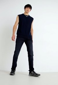 Top senza maniche di colore blu navy, jeans scuri e scarpe da ginnastica grigie; design minimalista e silhouette aderente con una texture liscia e uno stile casual.