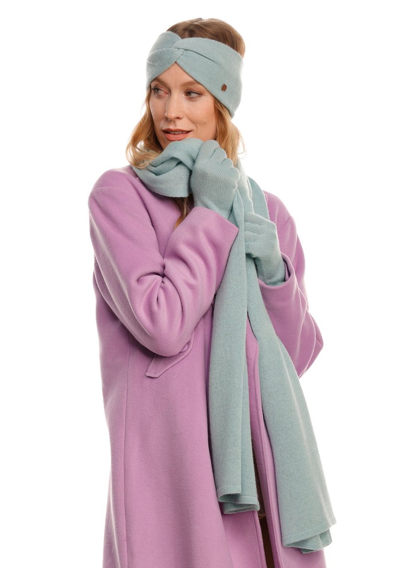 Fascia e sciarpa lavorate a maglia blu chiaro, con una consistenza morbida. Indossate con un cappotto di lana viola pastello, caratterizzato da un ampio colletto e tasche.