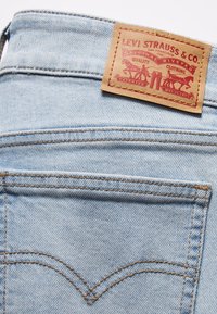Light blue denim fabric with contrasting brown stitching. Leather label attached at the waistband displaying "Levi Strauss & Co." logo and text.