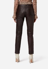 Bruine leren broek met een slim fit, met achterzakken en een soepele textuur, gecombineerd met lichtgekleurde hoge hakken.