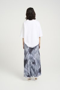 Camisa branca oversized com mangas curtas, combinada com uma saia longa e fluida que apresenta um padrão abstrato em cinza e preto.