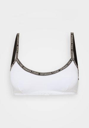 Valkoinen bralette mustilla hihnoilla. Sisältää logonauhan, jossa on teksti "Copenhagen Studios". Sujuva pinta ja yksinkertainen kupin muotoilu.